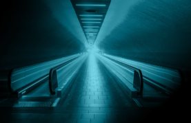 illuminated tunnel with moving walkways on either side moving towards a bright light at the end